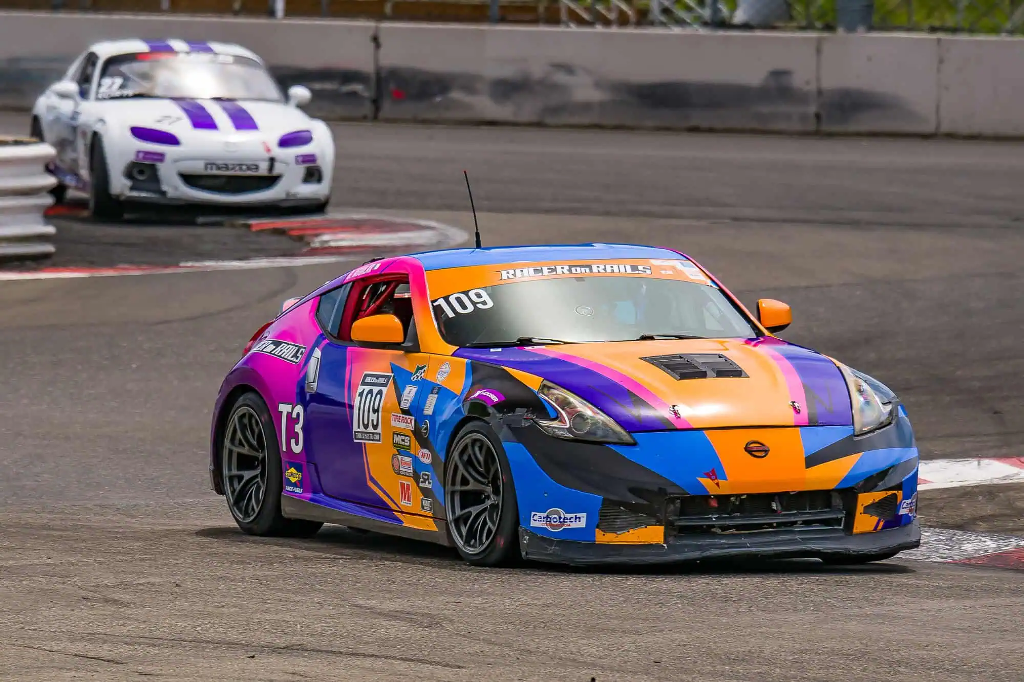 Gama Aguilar-Gamez driving the Racer on Rails Nissan 370Z Touring 3 race car through Portland International Raceway with a Spec MX-5 behind.