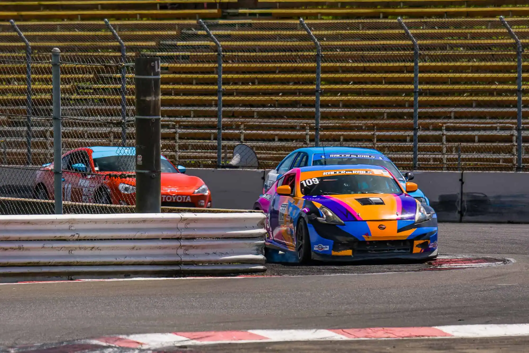 Racer on Rails Nissan 370Z Touring 3 race car driving over the curbing at Portland International Raceway with race traffic behind.  | (C) 2025 Doug Berger | DBPics