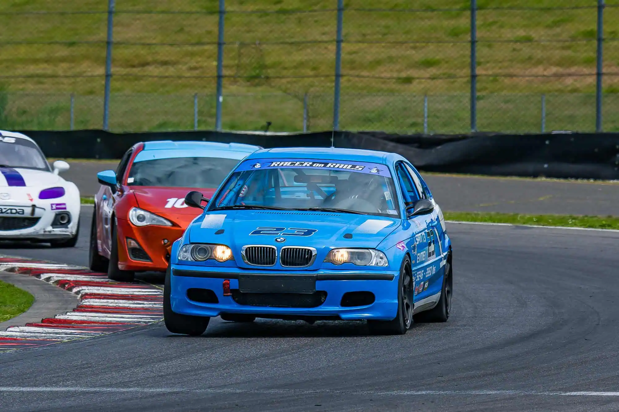 Chris Johnson driving the blue Racer on Rails BMW Spec E46 Touring 3 race car through Portland International Raceway with race traffic close behind.