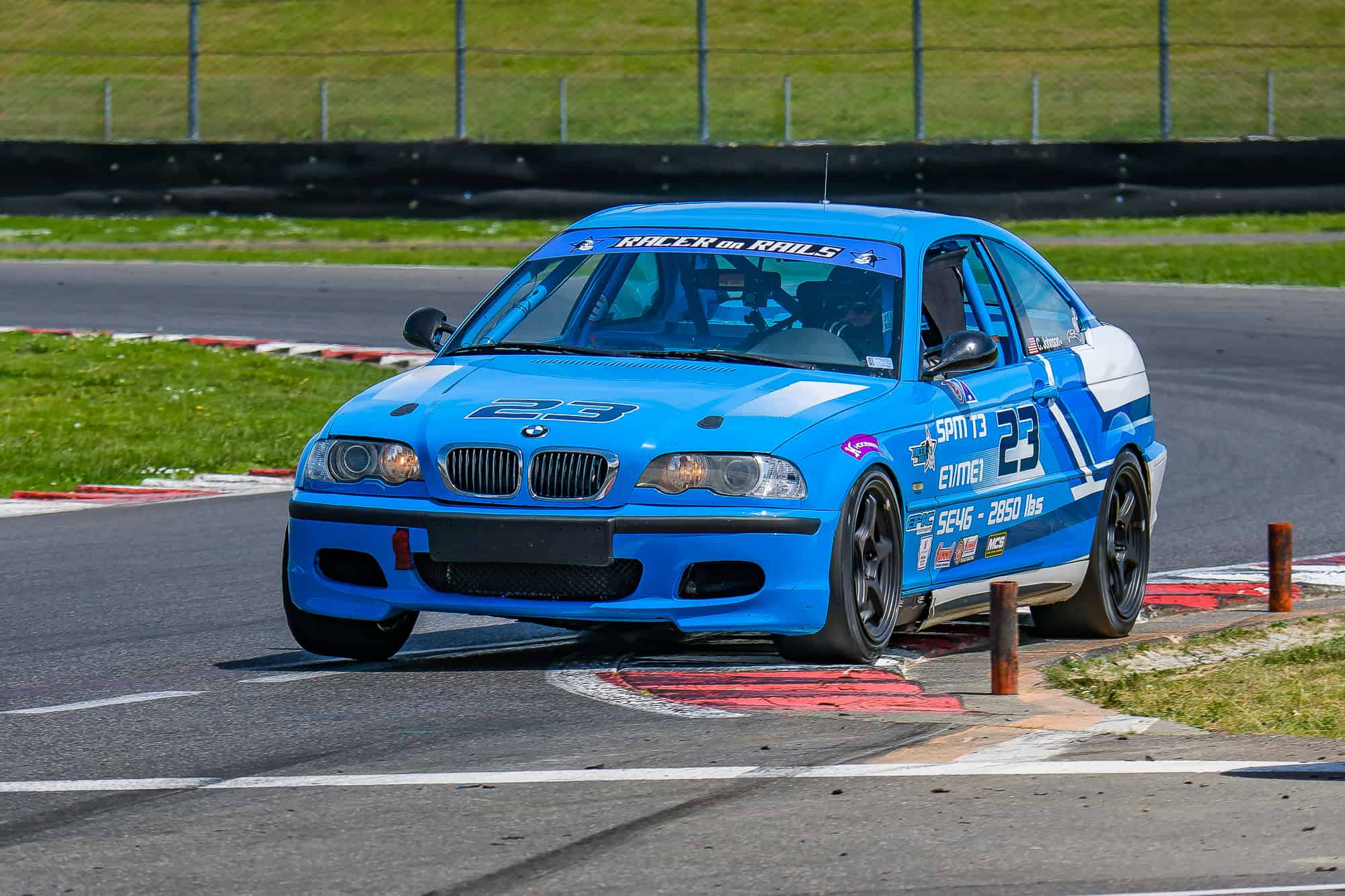 Blue Racer on Rails BMW Spec E46 Touring 3 race car using the curbing at Portland International Raceway during the Oregon SCCA Hoosier Super Tour.