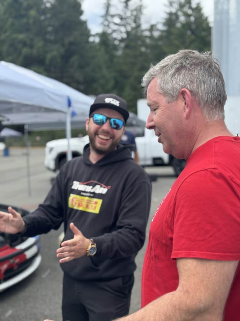 Tyler Campbell and Matt Dawson talk beside a race car in the Pacific Raceways paddock.